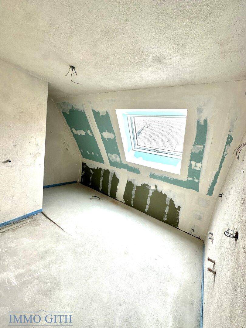 Dachgeschosszimmer im Rohbau mit großem Dachfenster, schrägen Wänden und viel natürlichem Licht.