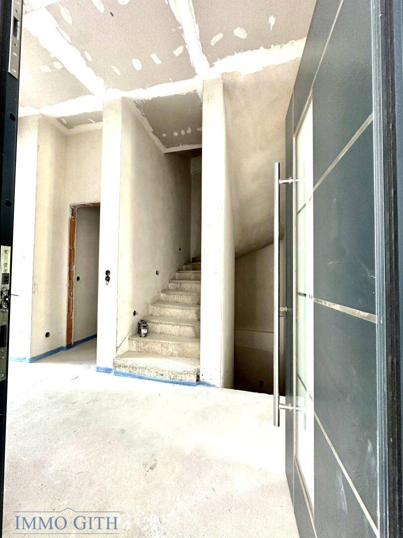 Eingangsbereich im Rohbau mit offener Treppe und Blick auf die noch unfertigen Wände und Decken.