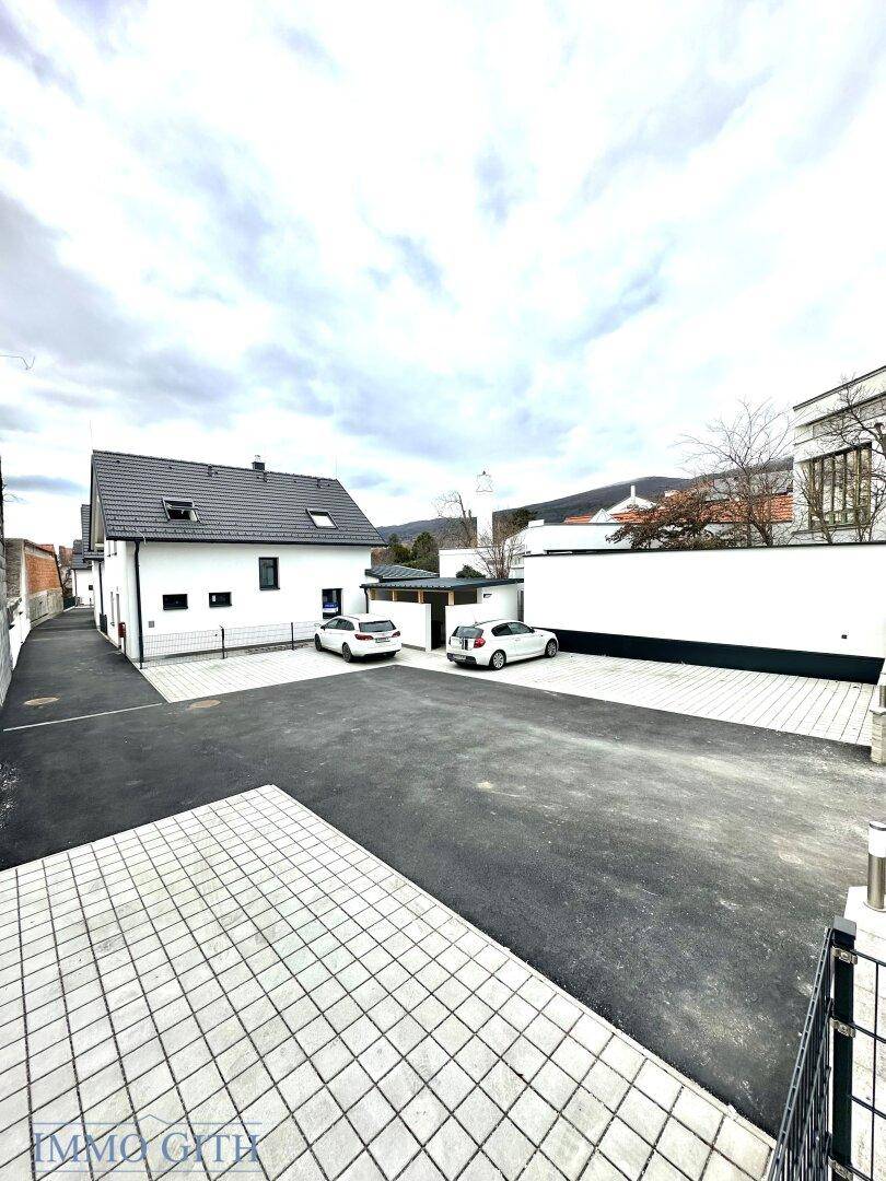 Ansicht des modernen Neubauhauses mit gepflastertem Vorplatz und Parkmöglichkeiten unter bewölktem Himmel.