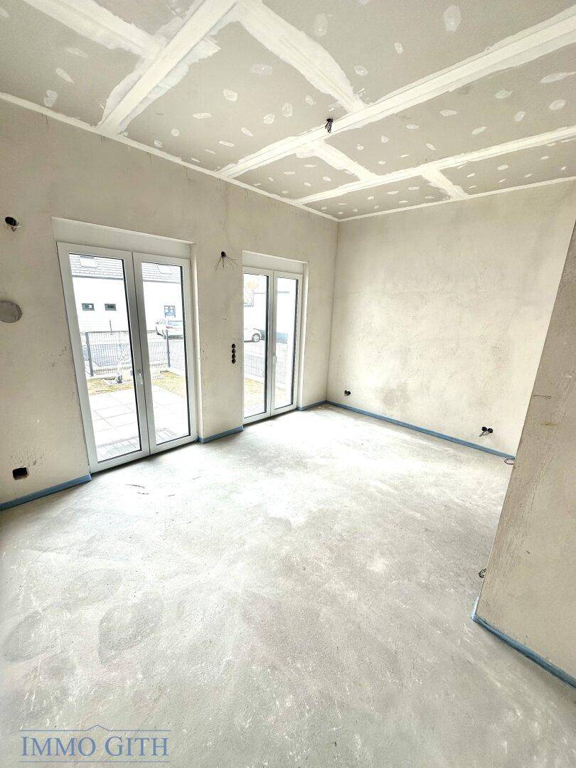 Unfertiger Innenraum mit großen Fenstertüren, bereit für den weiteren Ausbau und die Gestaltung.
