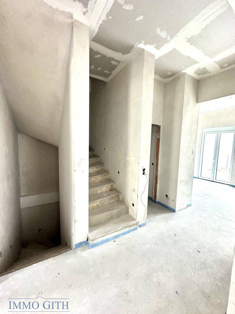 Unfertiger Flurbereich mit einer Treppe, die in ein weiteres Stockwerk führt, im Rohbauzustand.