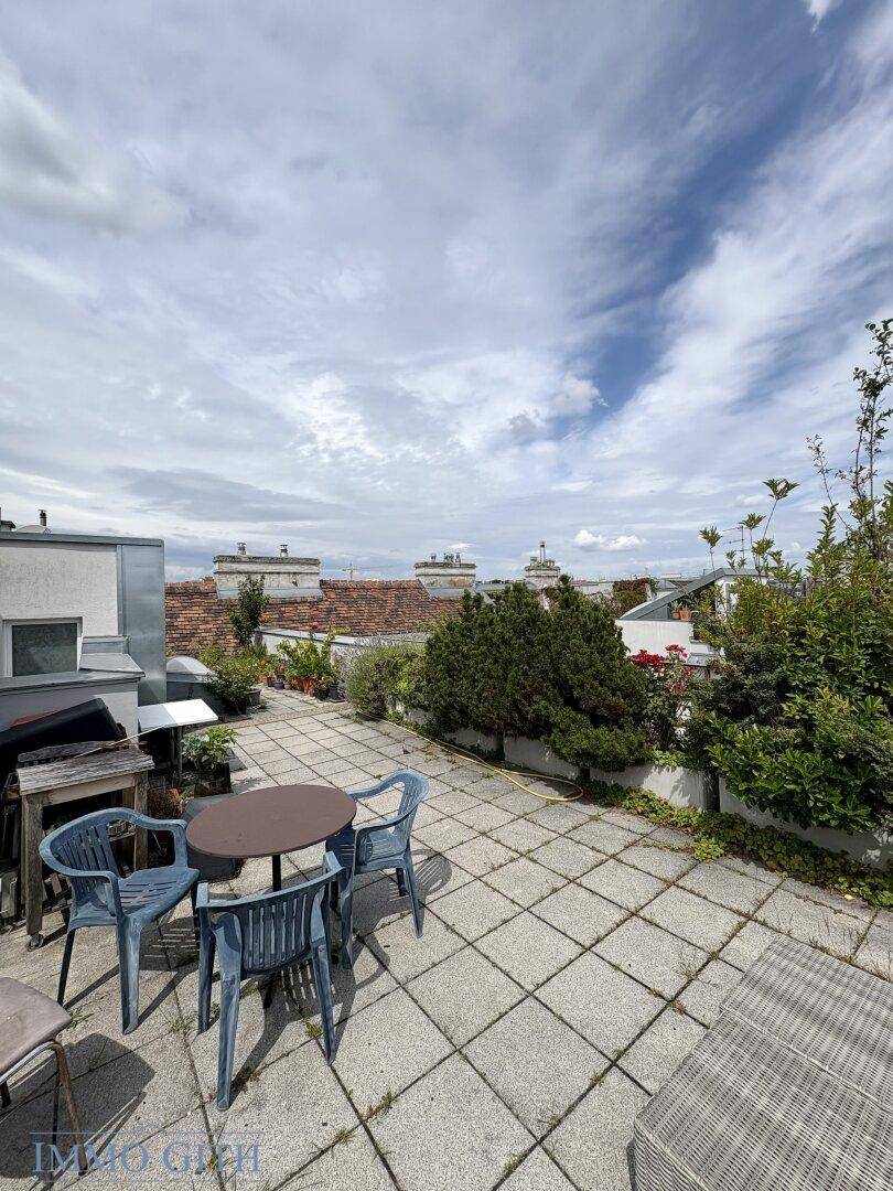 Große Dachterrasse mit Fliesenboden, Sitzgelegenheiten und Blick auf die umliegenden Gebäude.