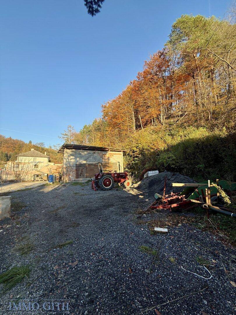 Ländliches Anwesen mit einem Schuppen, einem Traktor und Herbstbäumen im Hintergrund.