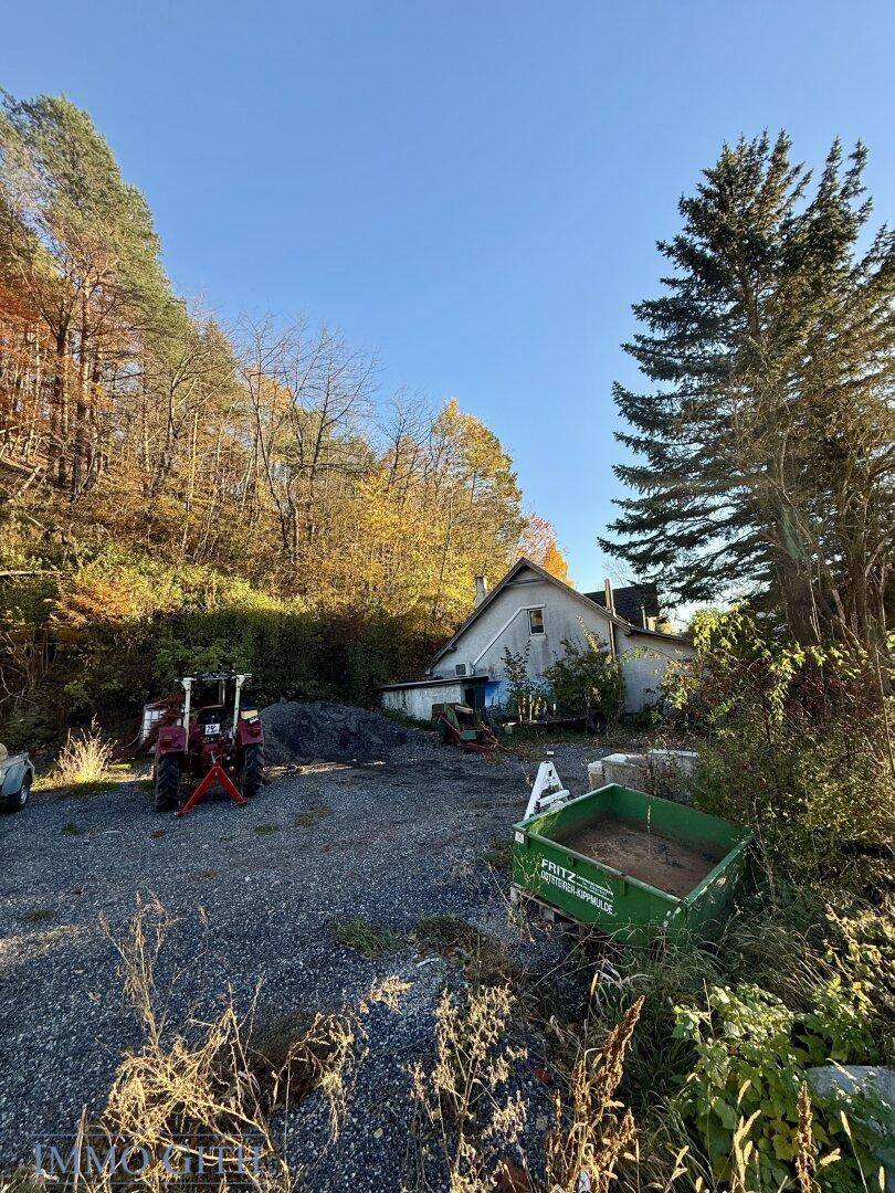 Ländliches Anwesen mit einem Haus, Schotterfläche und einem Traktor vor herbstlicher Kulisse.