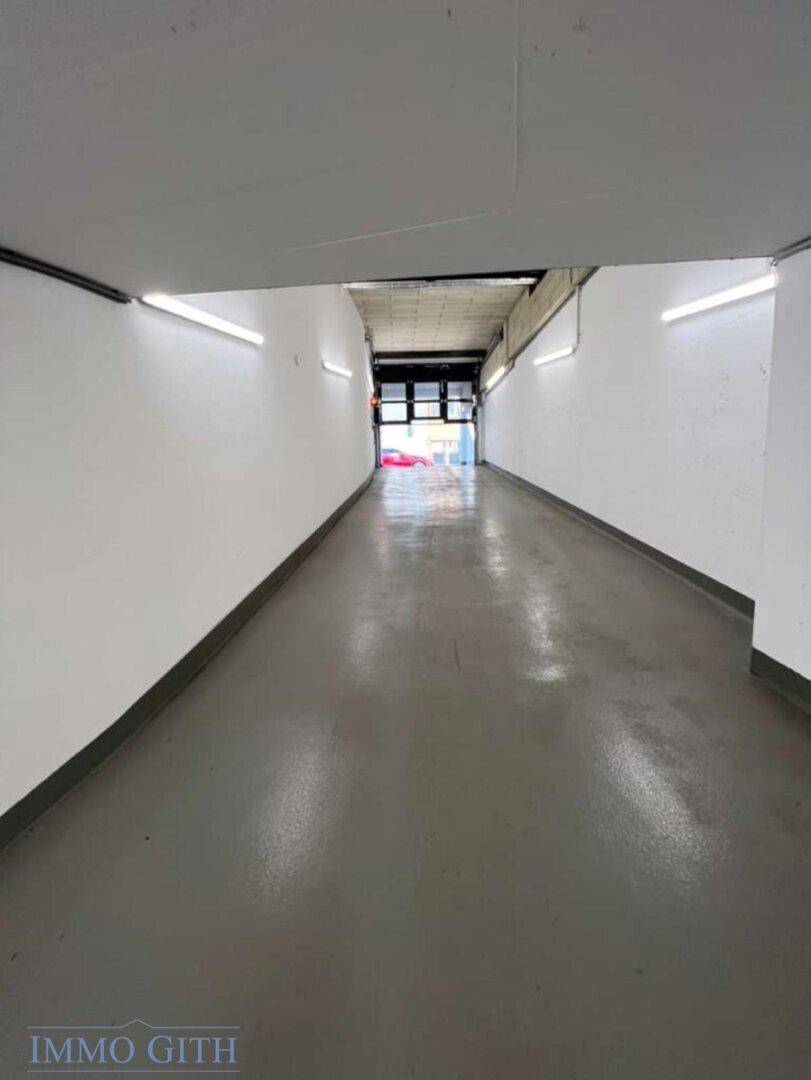 Langer, gut beleuchteter Gang in der Tiefgarage mit glattem Betonboden und weißen Wänden.