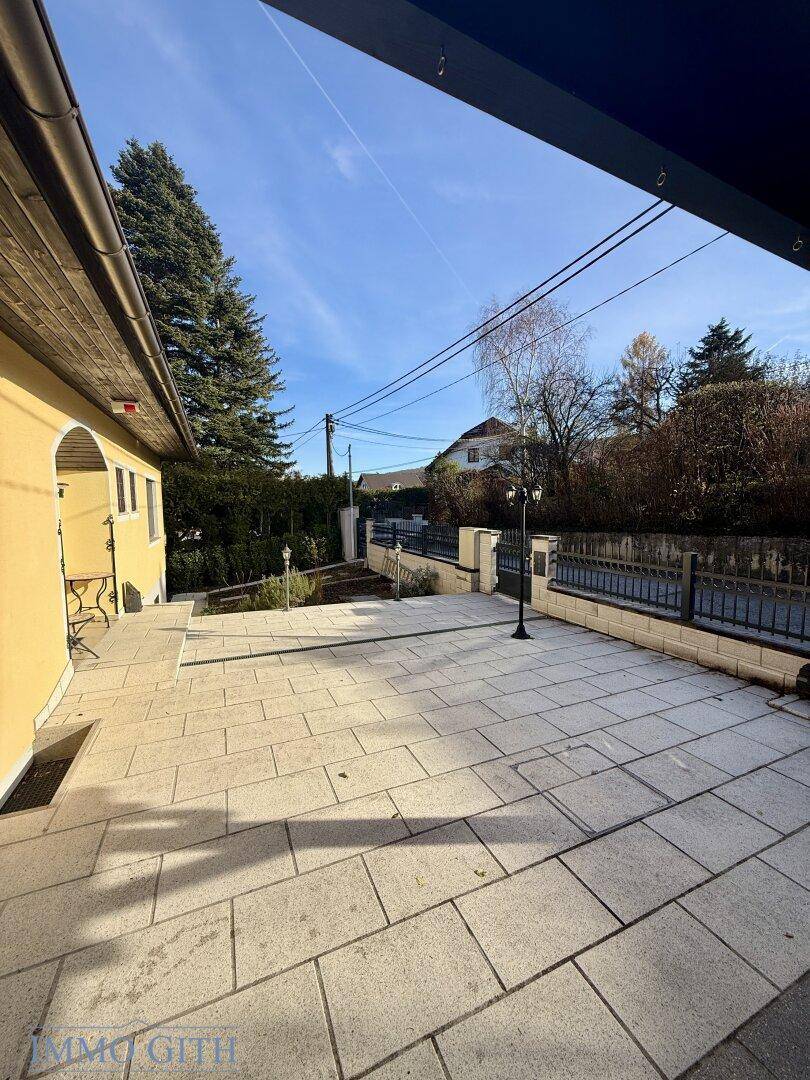 Große gepflasterte Terrasse vor dem Haus mit sonnigem Ausblick.
