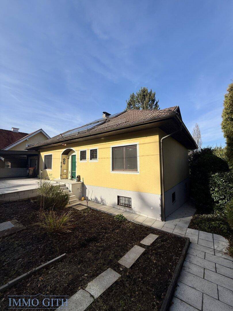 Seitenansicht des gelben Hauses mit Photovoltaikanlage und kleinem Gartenbereich.