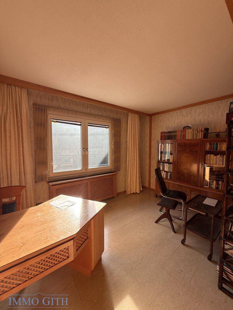 Helles Arbeitszimmer mit Holzschreibtisch, Bücherregal und Blick ins Freie.