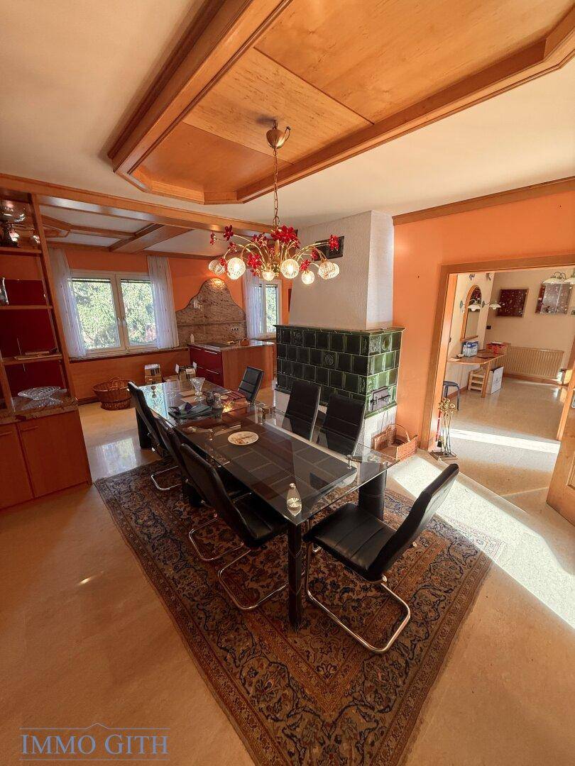 Großer Essbereich mit Kachelofen, Holzbalkendecke und Blick in den Garten.