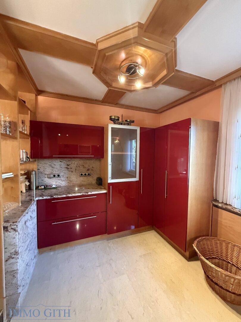 Winkelküche mit roten Hochglanzschränken, Granitflächen und Holzdecke im Landhausstil.