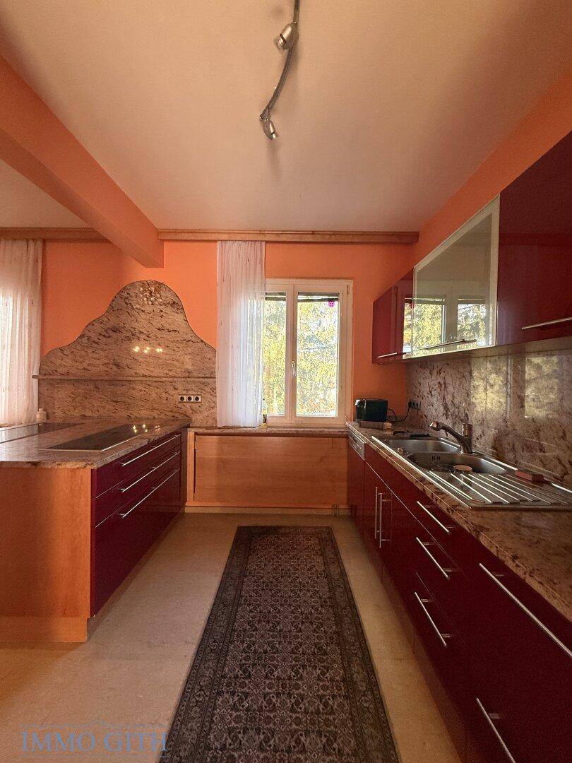 Moderne Küche mit roten Hochglanzfronten, Granitarbeitsplatten und Fensterblick ins Grüne.