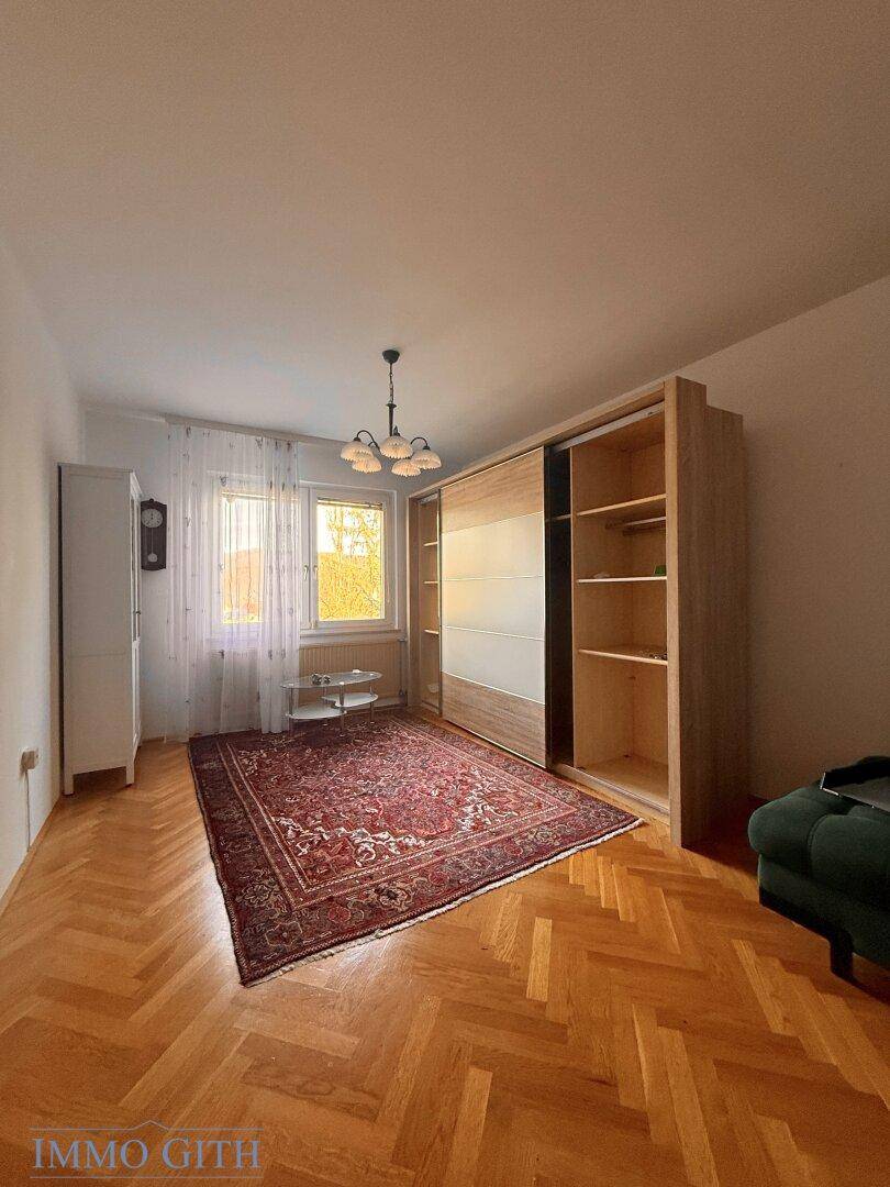 Schlafzimmer mit Fischgrätparkett, großem Schiebetürenschrank und Fenster mit viel Tageslicht.