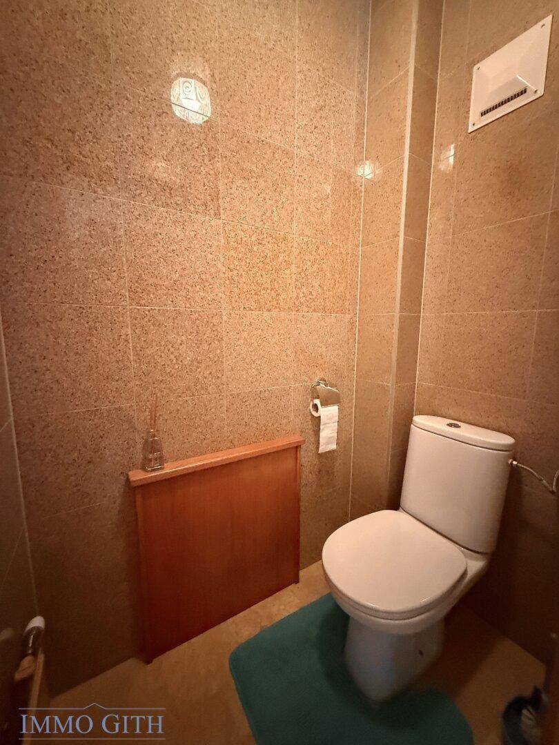 Separate Toilette mit Fliesenboden und Wandverkleidung in warmen Brauntönen.