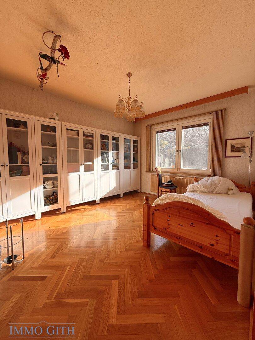 Helles Schlafzimmer mit Fischgrätparkett, weißen Einbauschränken und Holzdoppelbett.