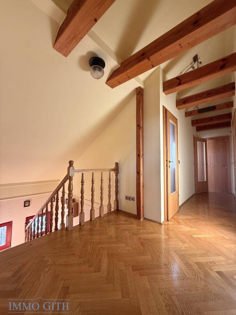 Dachgeschossflur mit sichtbaren Holzbalken, Fischgrätparkett und Zugang zu weiteren Räumen.