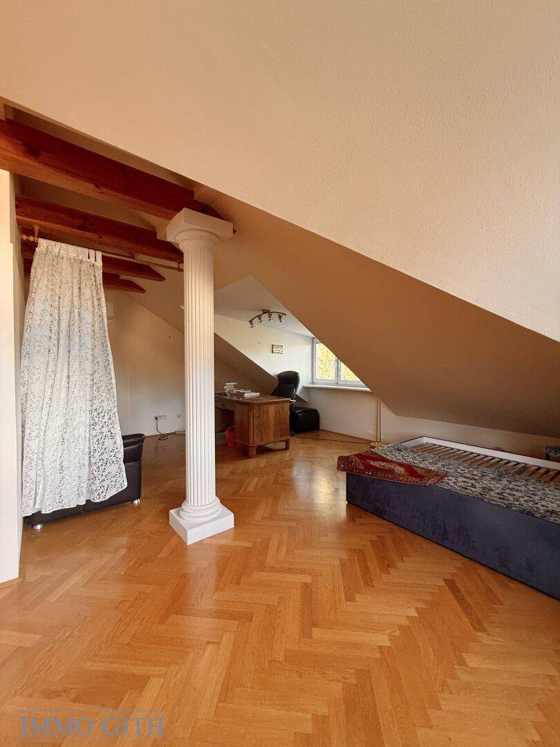 Geräumiges Dachzimmer mit Fischgrätparkett, dekorativer Säule und schrägen Wänden.
