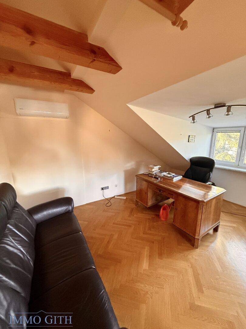 Dachzimmer mit Fischgrätparkett, Schreibtischbereich und Klimaanlage unter der Dachschräge.