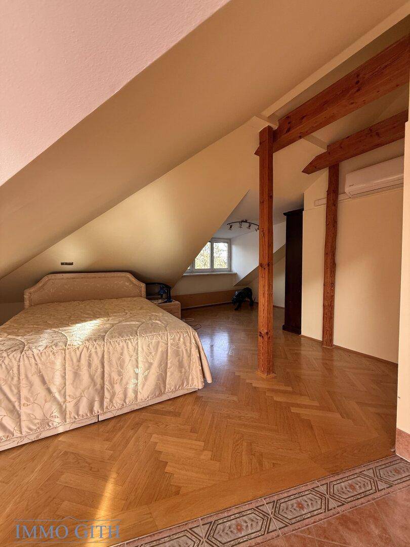 Dachzimmer mit Fischgrätparkett, Holzbalken und Bett unter der Dachschräge.