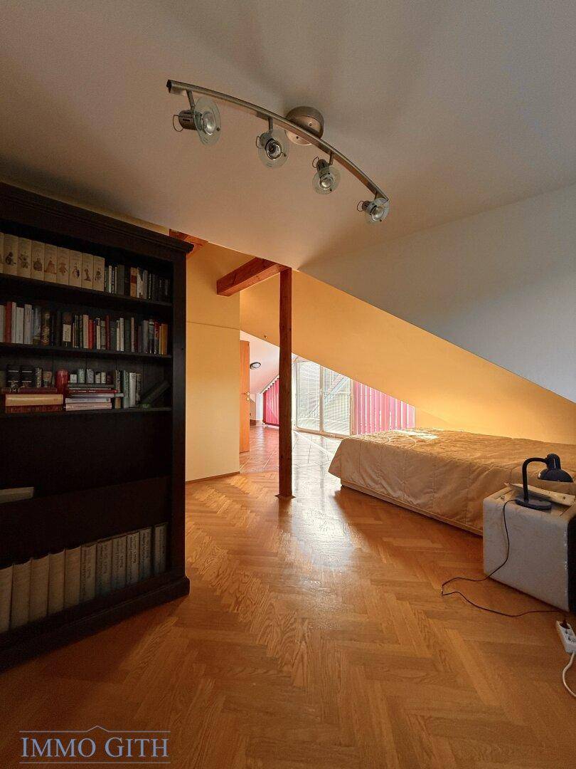 Dachzimmer mit Fischgrätparkett, Bücherregal und Bett unter der Dachschräge.