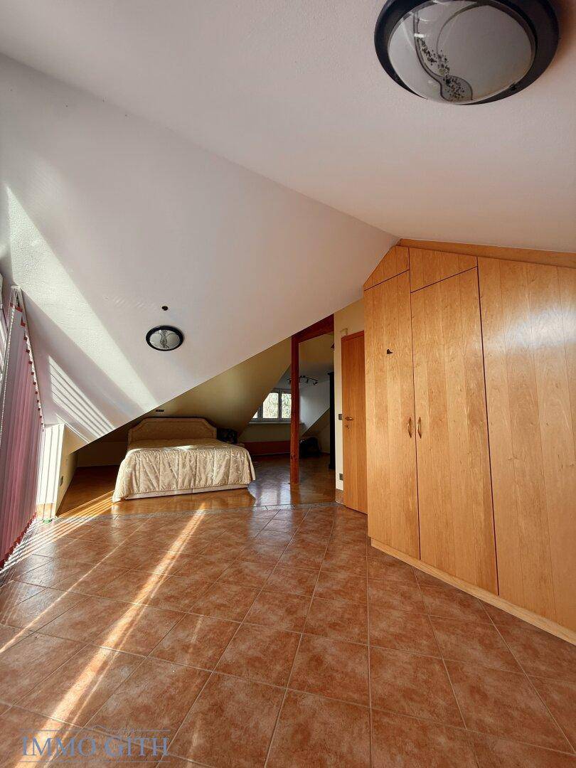 Dachzimmer mit Fliesenboden, Einbauschrank und Bett unter der Dachschräge.