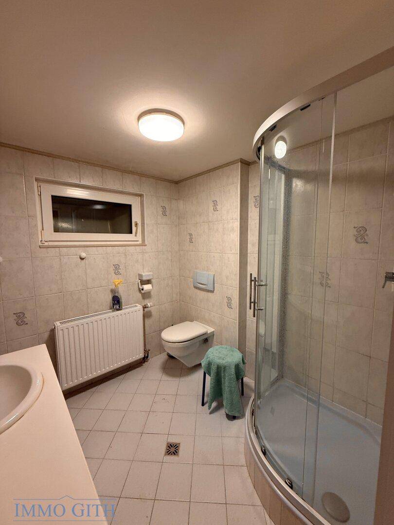 Badezimmer mit Duschkabine, WC, Waschbecken und Fenster.