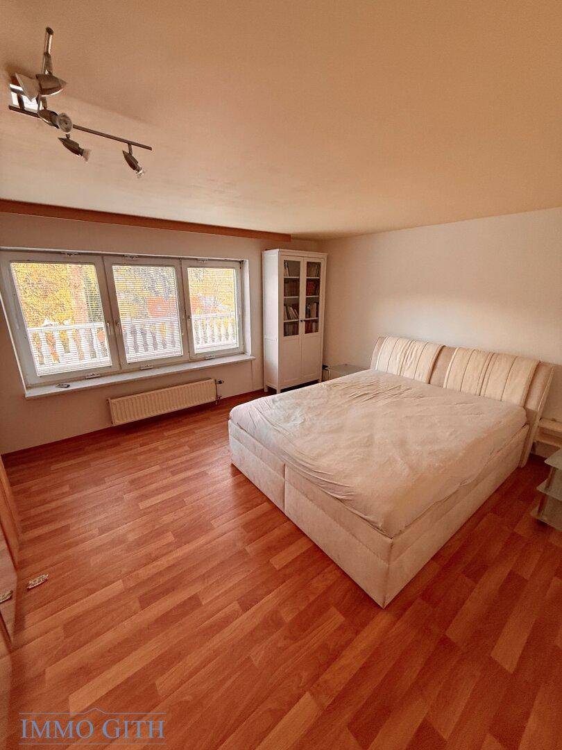 Geräumiges Schlafzimmer mit Holzboden, großem Doppelbett und Fenster mit Blick ins Grüne.