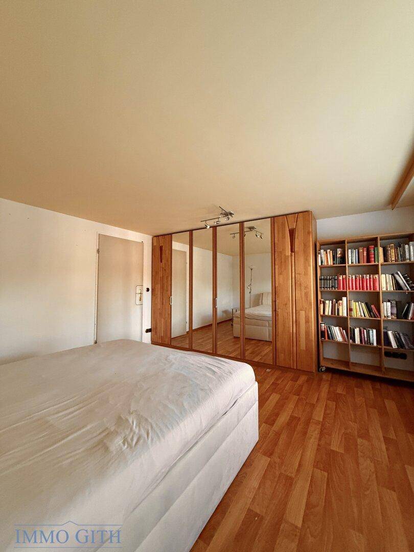 Helles Schlafzimmer mit Holzboden, Spiegelschränken und einem Bücherregal.