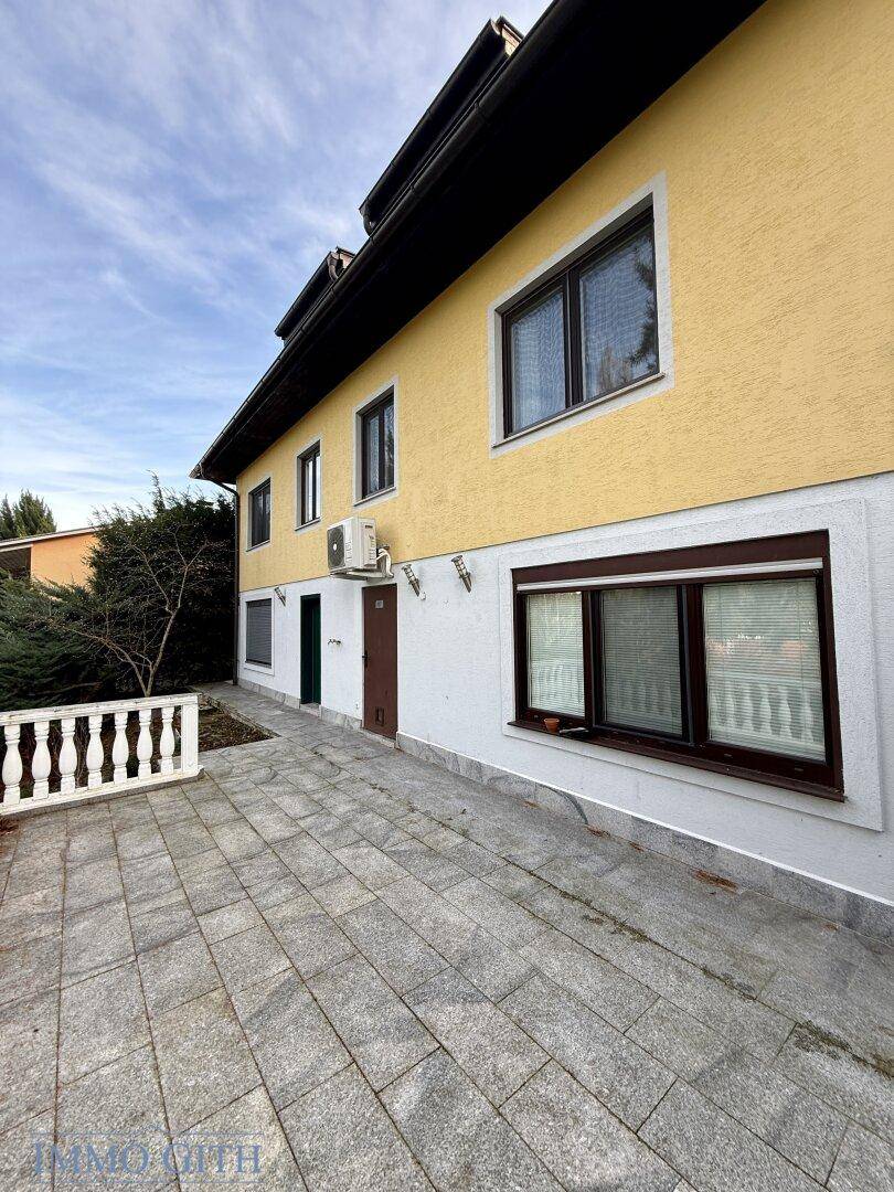Seitenansicht des Hauses mit gepflastertem Bereich und Klimaanlage.