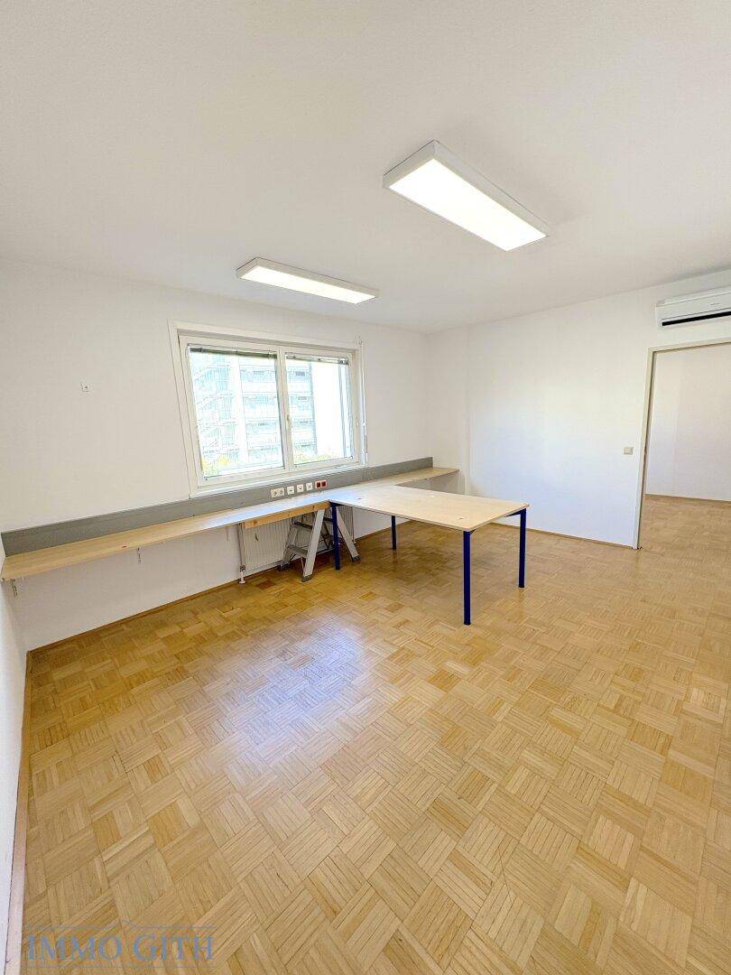 Büroraum mit Holzboden, Fenster und Klimaanlage, ausgestattet mit langen Arbeitsflächen.