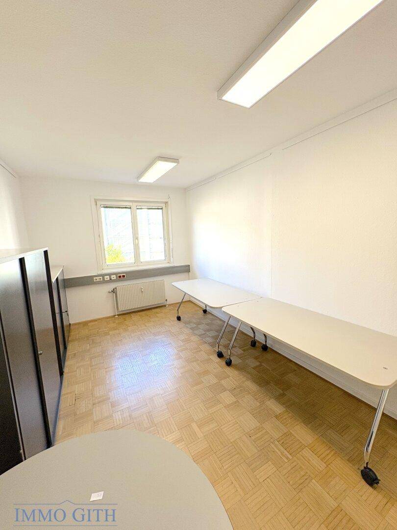 Heller Büroraum mit Holzboden, Fenster und grauen Schränken, ideal für Teamarbeit.