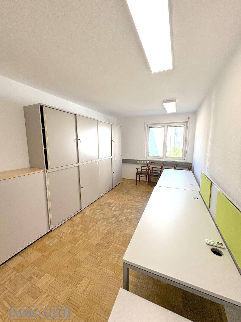 Büroraum mit Holzboden, Fenster und langen Schreibtischen, ausgestattet mit Stauraum.
