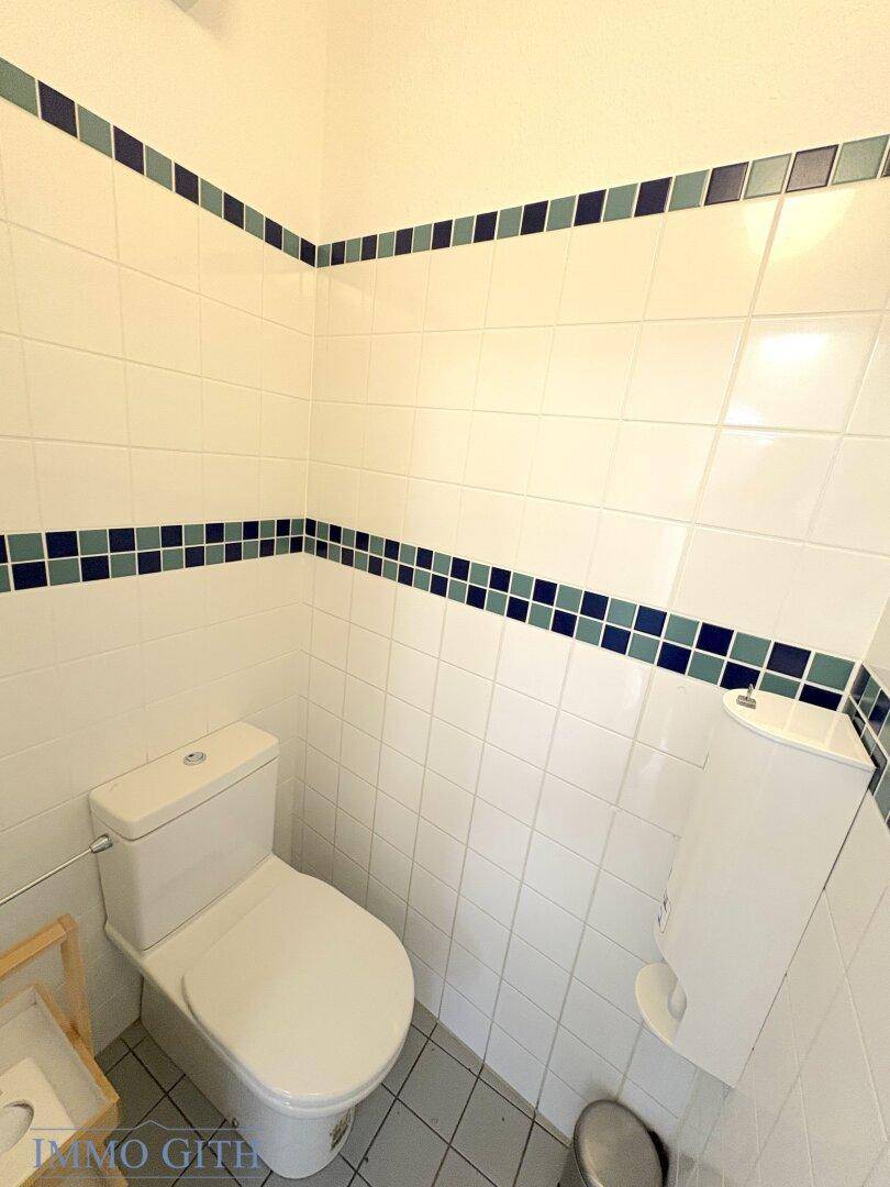 Saubere Gästetoilette mit WC, weißen Fliesen und blauen Dekorstreifen.