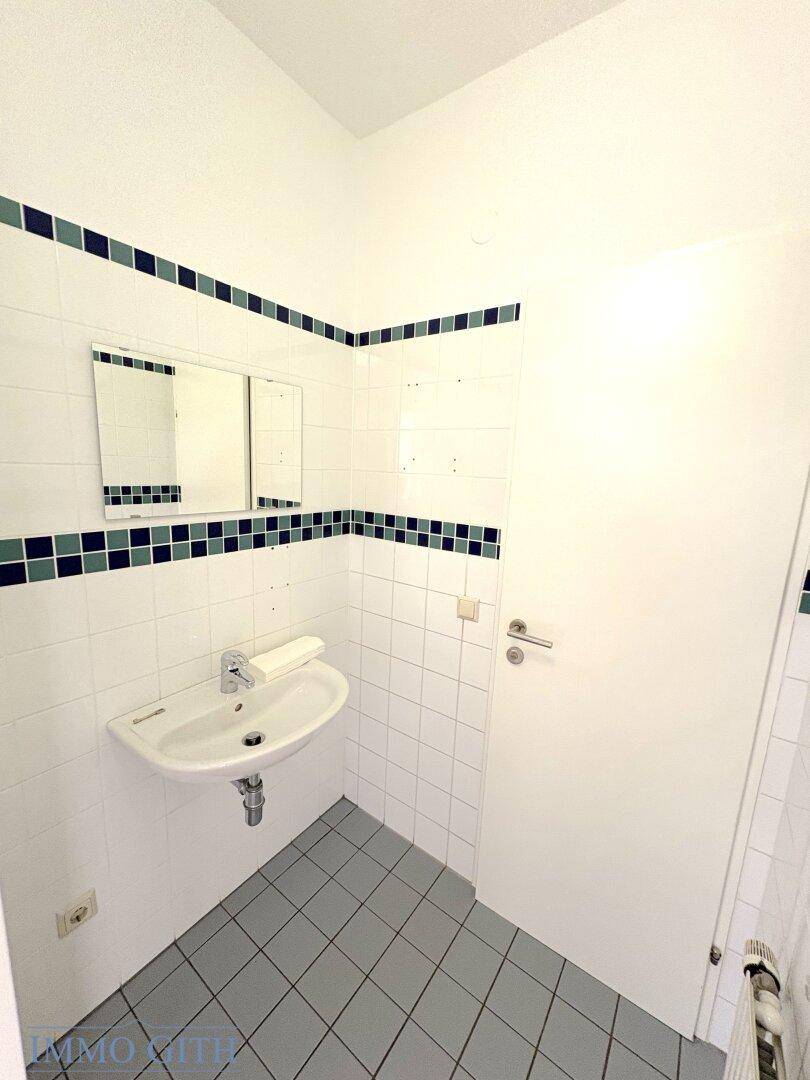 Einfache Gästetoilette mit Waschbecken, weißen Fliesen und dekorativen blauen Akzenten.