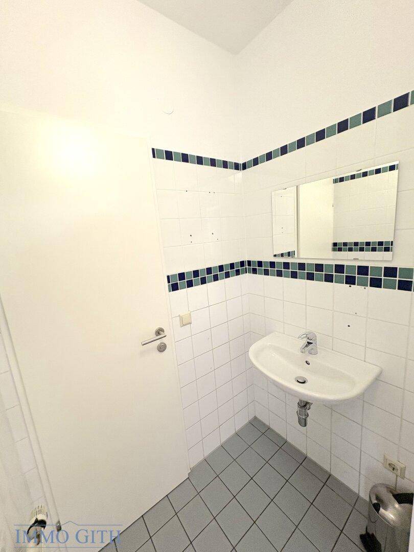Funktionale Gästetoilette mit Waschbecken, Spiegel und weißen Fliesen mit blauen Akzenten.