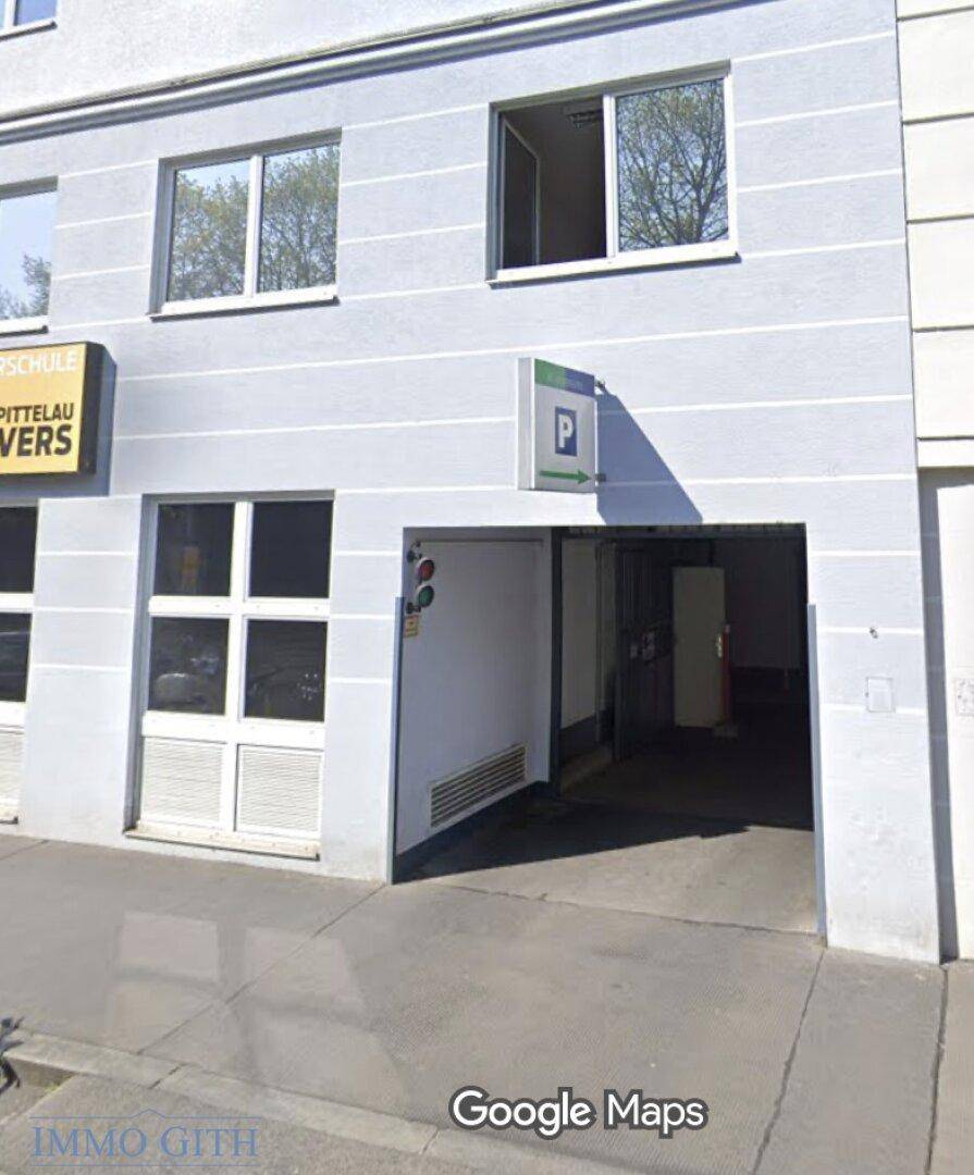 Eingang einer Tiefgarage mit Rampe und modernen Fenstern an der Gebäudefassade.