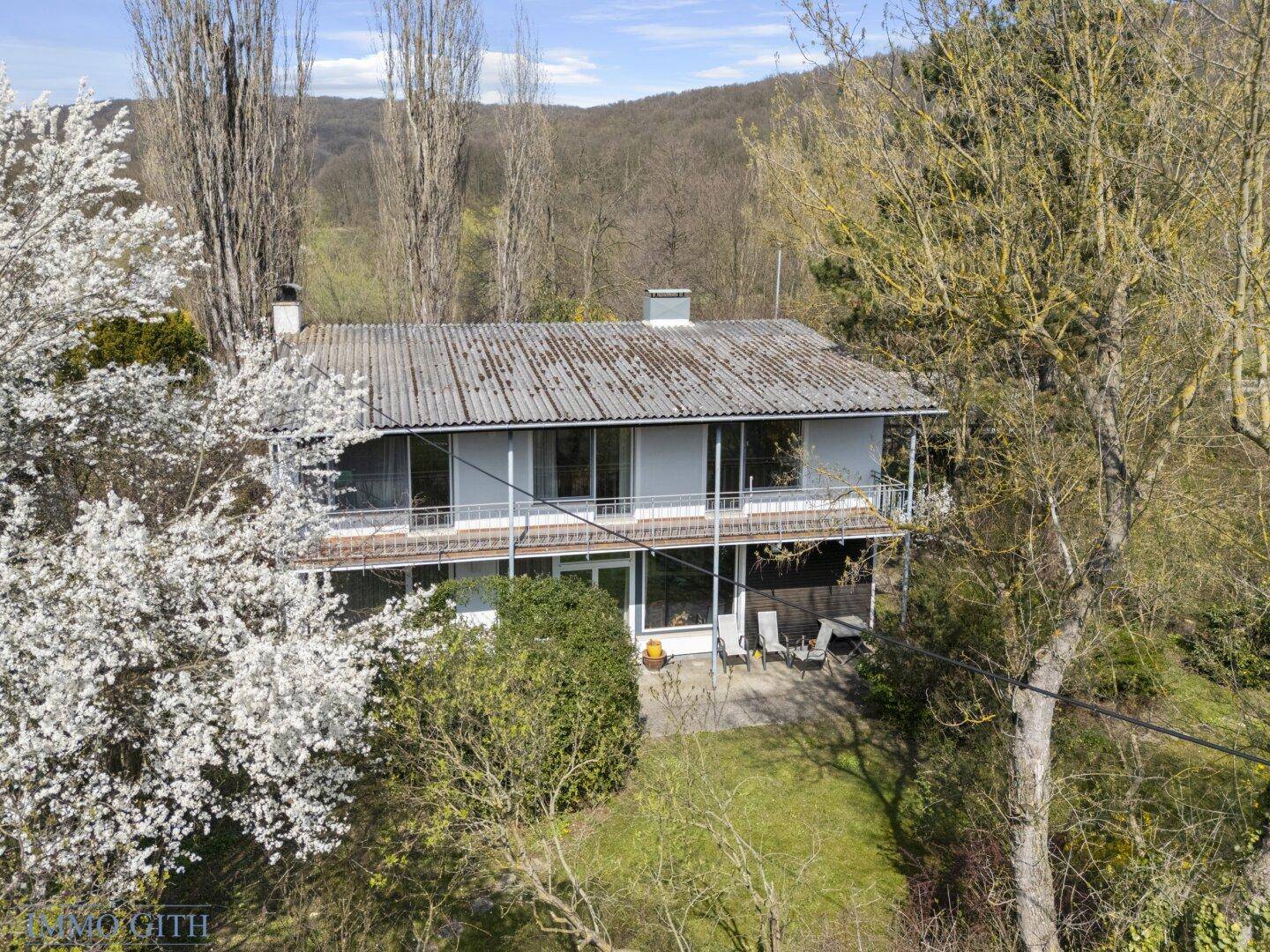 Luftaufnahme des Hauses mit Balkonen und umliegender grüner Landschaft unter hellem Himmel.