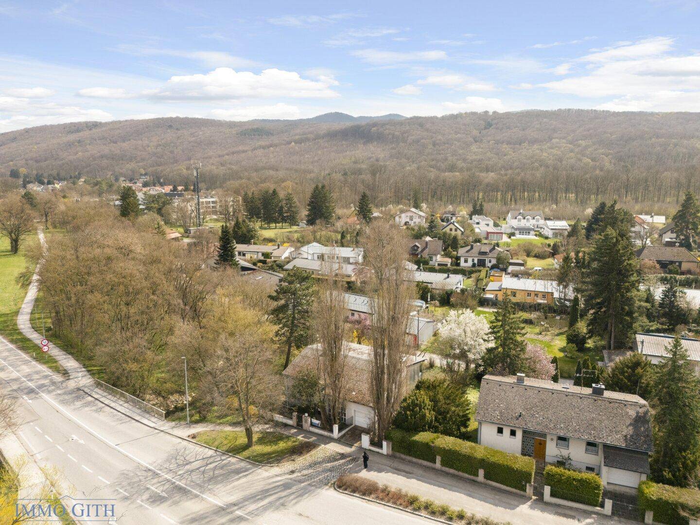 Weitläufige Ansicht der Wohnsiedlung mit Häusern, Straßen und bewaldeten Hügeln im Hintergrund.