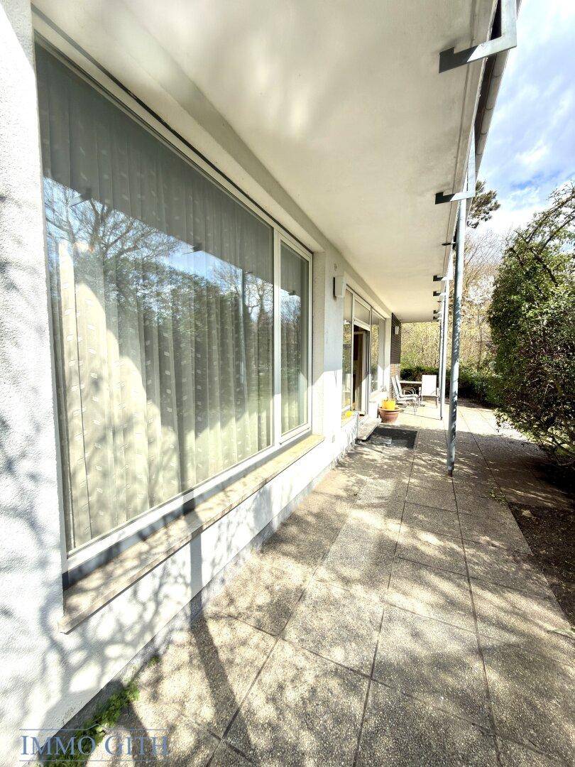Langer, überdachter Terrassenbereich entlang der Hausfassade mit großen Fenstern und Fliesenboden.