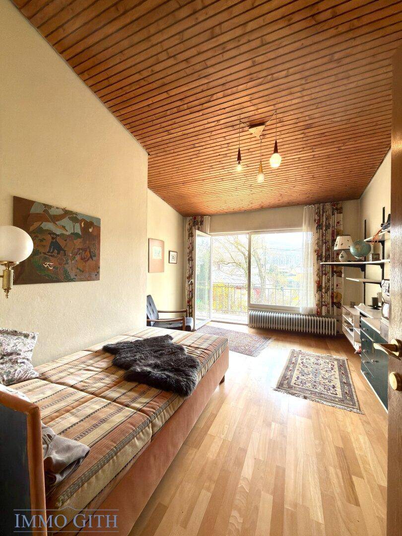 Gemütliches Zimmer mit Holzdecke, Parkettboden und großem Fenster mit Blick ins Grüne.