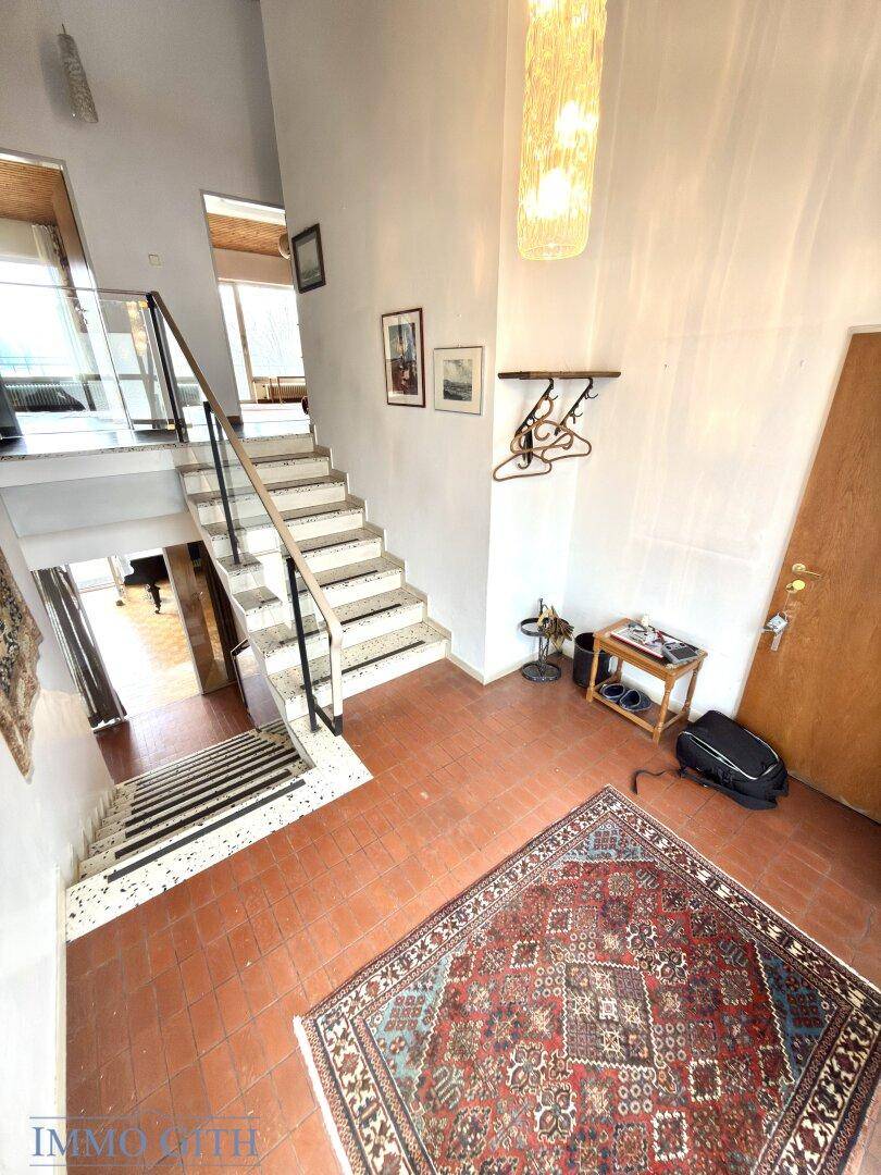 Heller Eingangsbereich mit Terrakottafliesen, Treppe und einem dekorativen Kronleuchter.