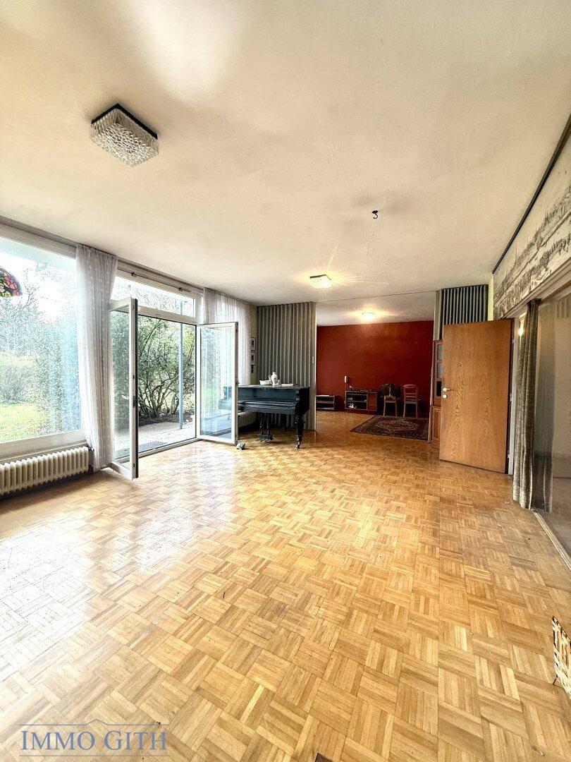 Großes Wohnzimmer mit Parkettboden, Klavier und Zugang zum Garten durch breite Türen.