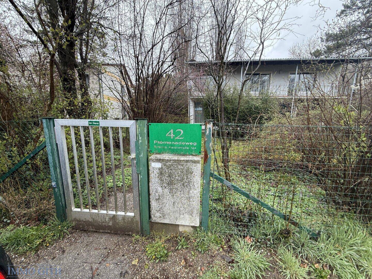 Eingangsbereich des Grundstücks mit grünem Straßenschild und Metalltor.
