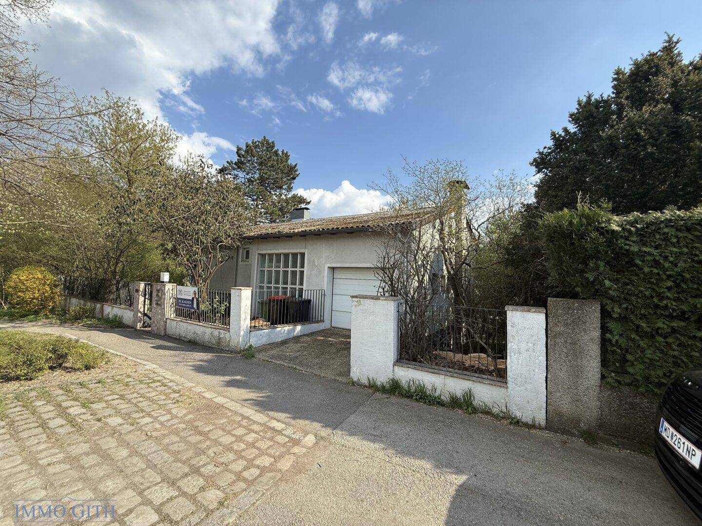 Vorderansicht des Hauses mit Garage, Einfahrt und Zaun an einem sonnigen Tag.