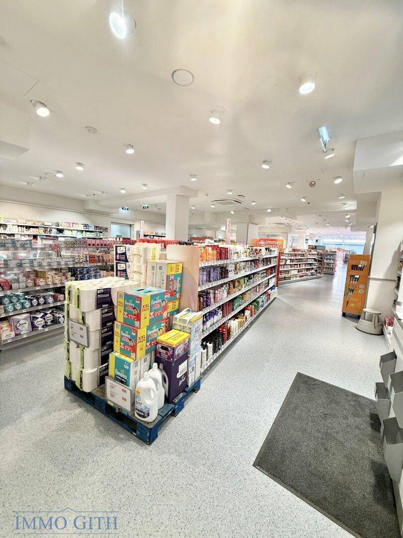 Innenansicht eines Einzelhandelsgeschäfts mit Produktpräsentationen und breiten Gängen.