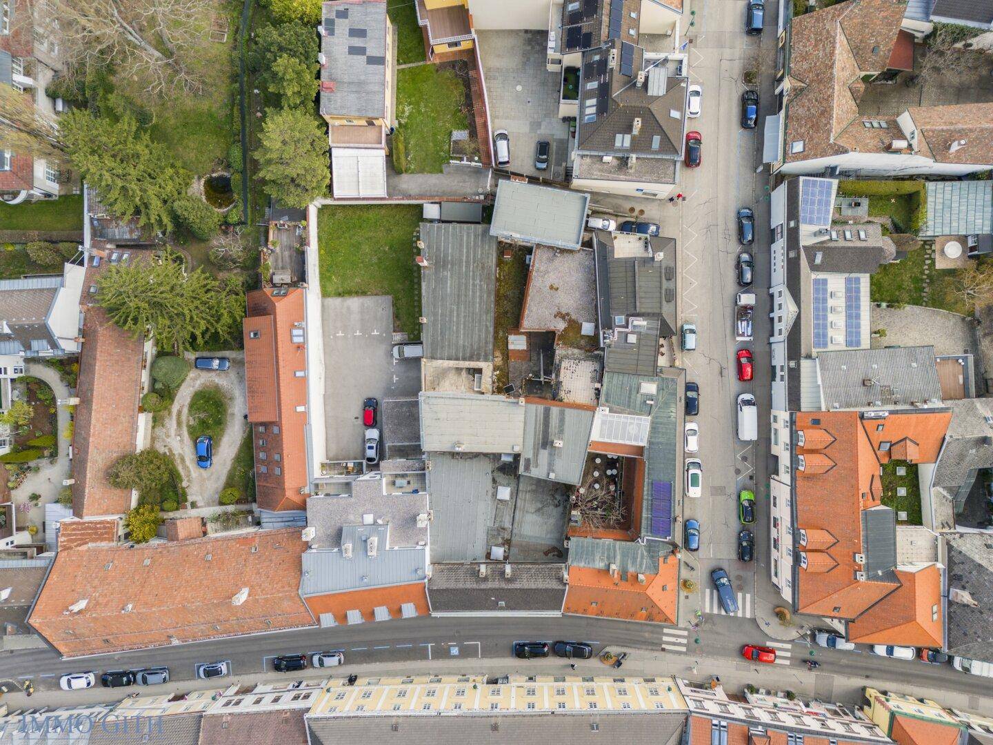 Luftaufnahme des Gebäudekomplexes mit umliegenden Häusern, Dächern und einem grünen Innenhof.