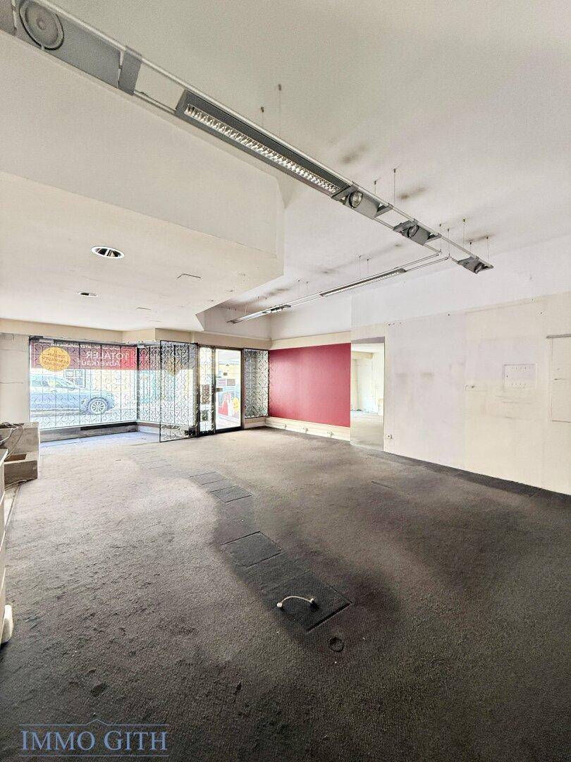 Großer, leerer Geschäftsraum mit Teppichboden, hohen Decken und roter Akzentwand.