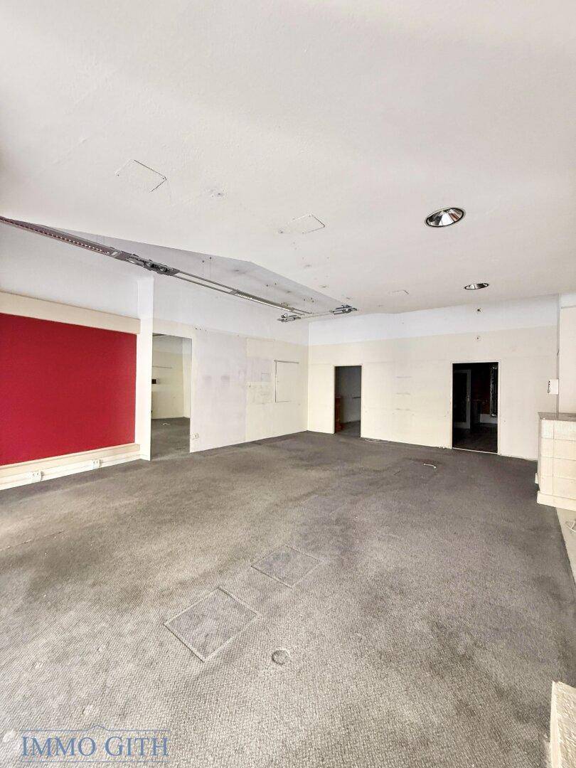 Weiter Blick in einen leeren Geschäftsraum mit Teppichboden und einer roten Wand.