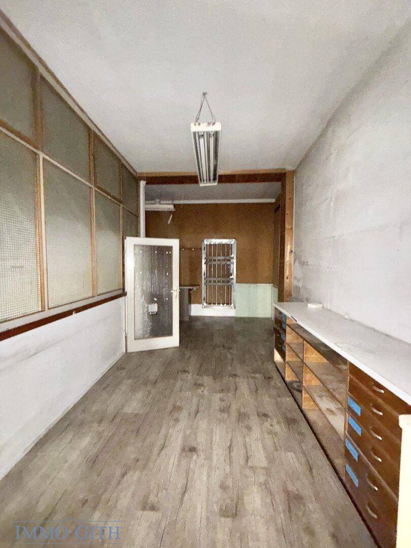 Langer Raum mit Holzoptik-Boden, einer Theke und einem Fenster zur Straße.