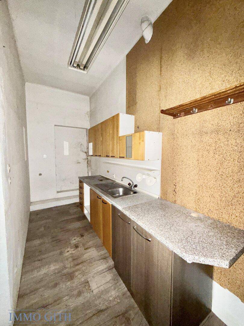 Einfacher Raum mit Spüle, Arbeitsplatte und Holzschränken, möglicherweise eine kleine Küche.