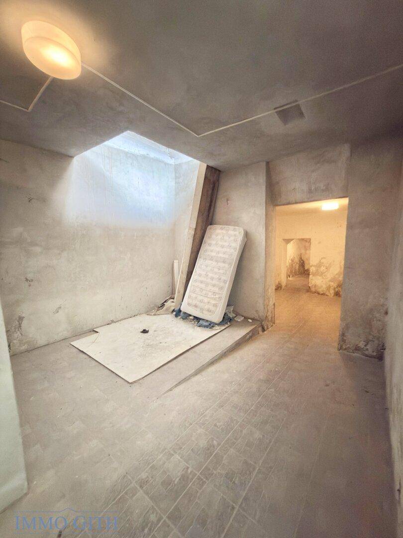 Unfertiger Raum im Untergeschoss mit Betonboden und einer Matratze an der Wand.